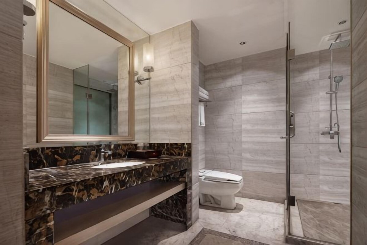 A modern bathroom with a marble vanity, a large mirror, a toilet, and a glass-enclosed shower area.