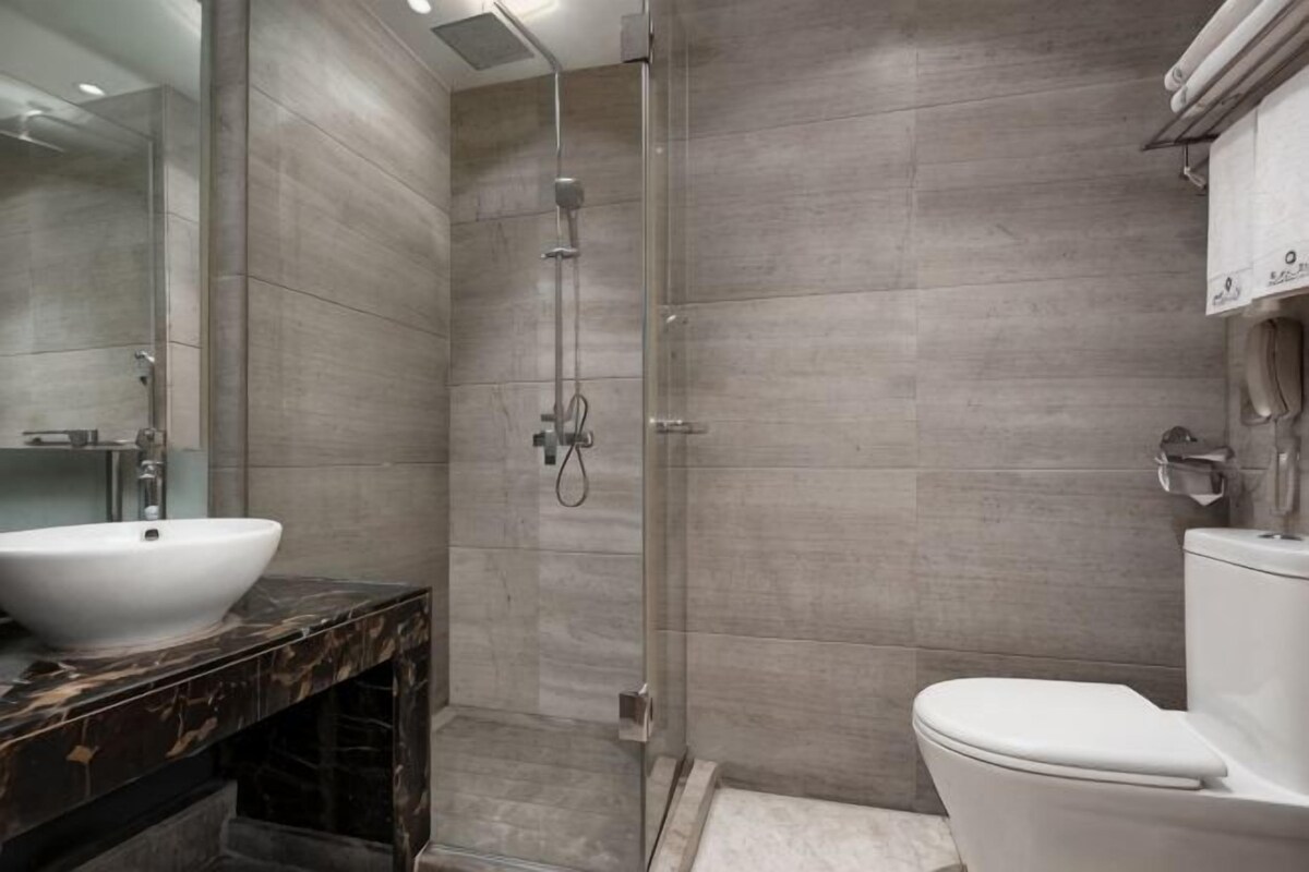 A modern bathroom with a large white sink, a glass-enclosed shower, and a toilet.