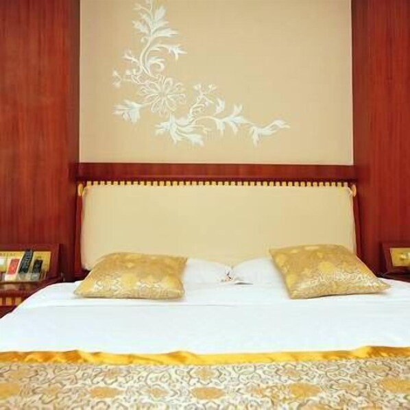 A hotel room with a bed, two pillows, a nightstand, and a wall with a floral design. - Peng JI Hotel (Xishuangbanna Dai)