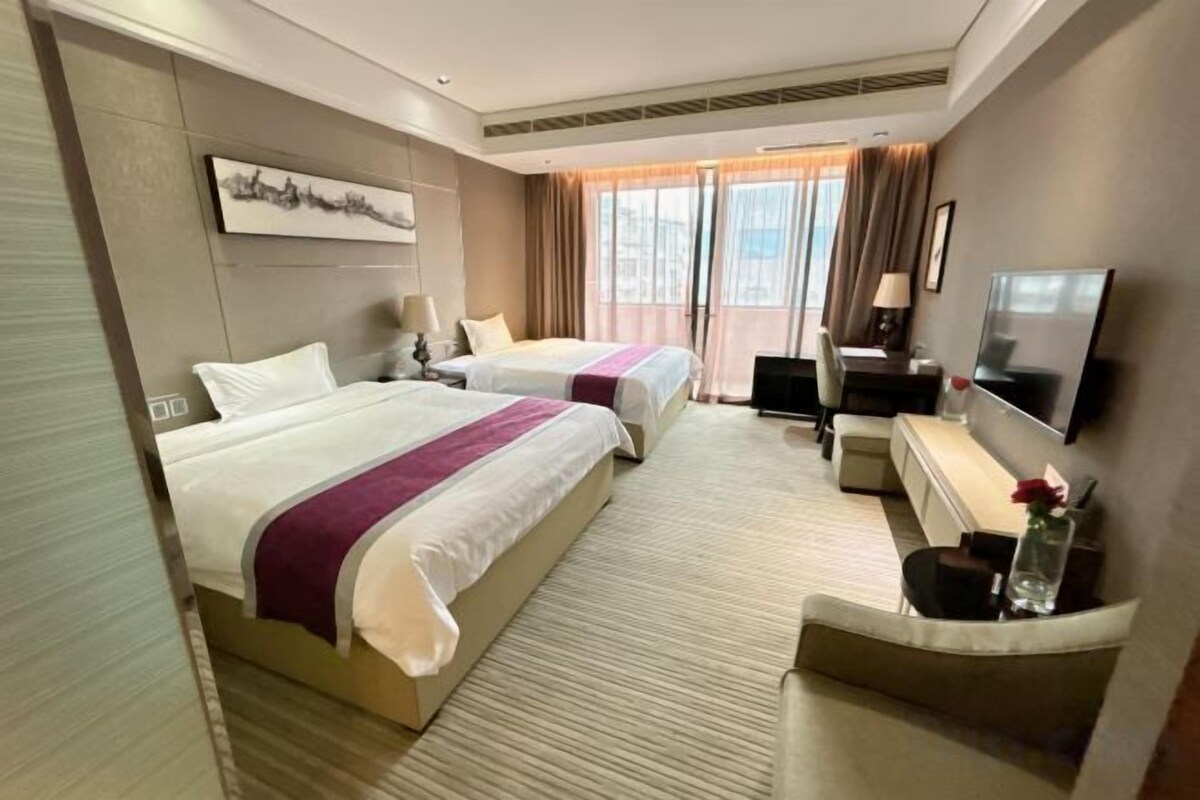 Una habitación de hotel con dos camas, un escritorio, un televisor y un ventanal con cortinas.