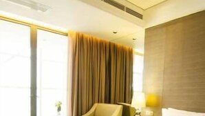 A hotel room with a large bed, a chair, a small table, and a window with curtains. - Bahao Gongguan Hotel (Dongguan)