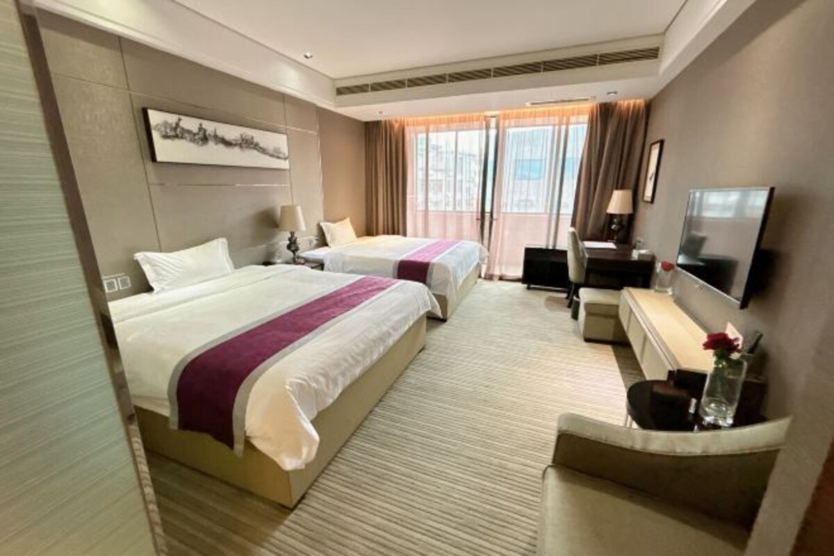 Habitación de hotel con dos camas, un escritorio, televisor y un ventanal con cortinas.