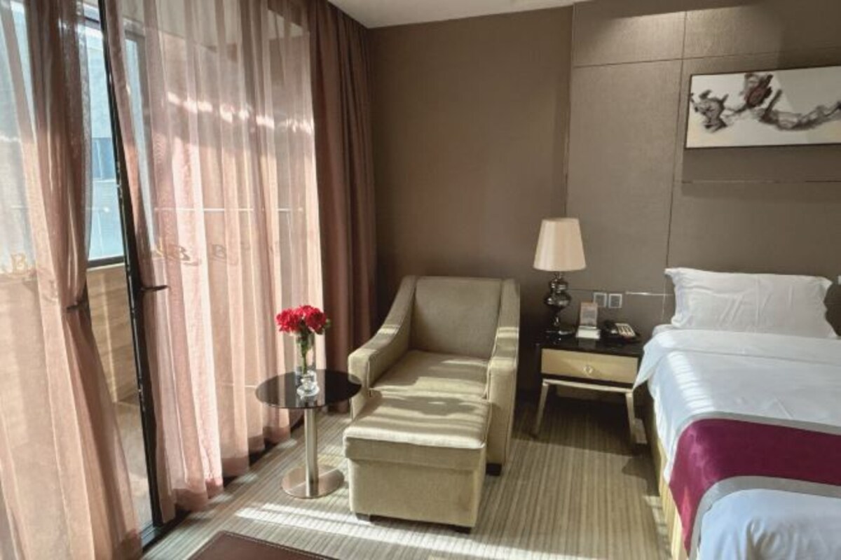 Una habitación de hotel con una cama, un sofá, una mesita de noche, una lámpara y una mesa con un jarrón de flores.
