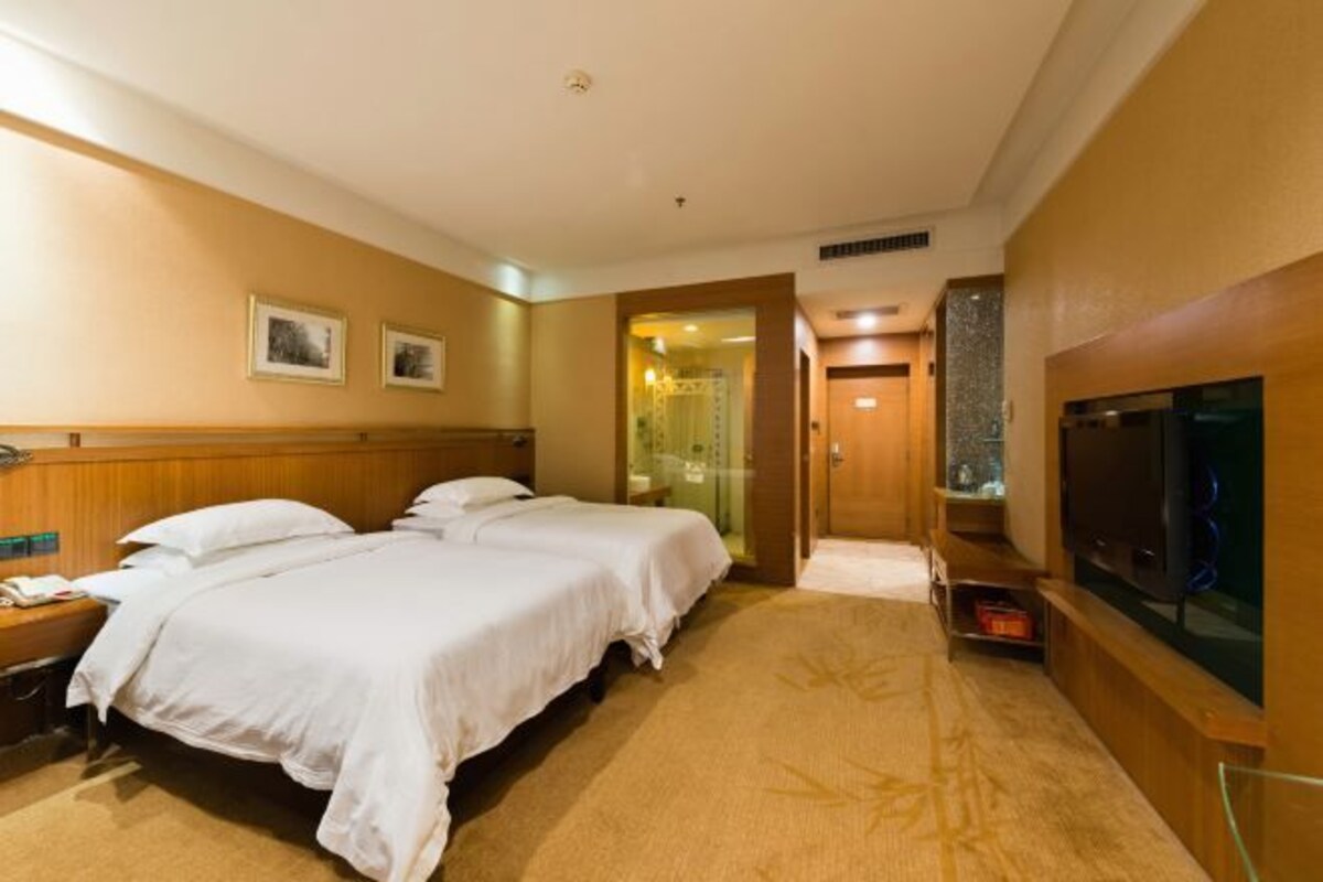 Une chambre d’hôtel avec deux lits, une télévision et une salle de bain visible à travers une porte ouverte.