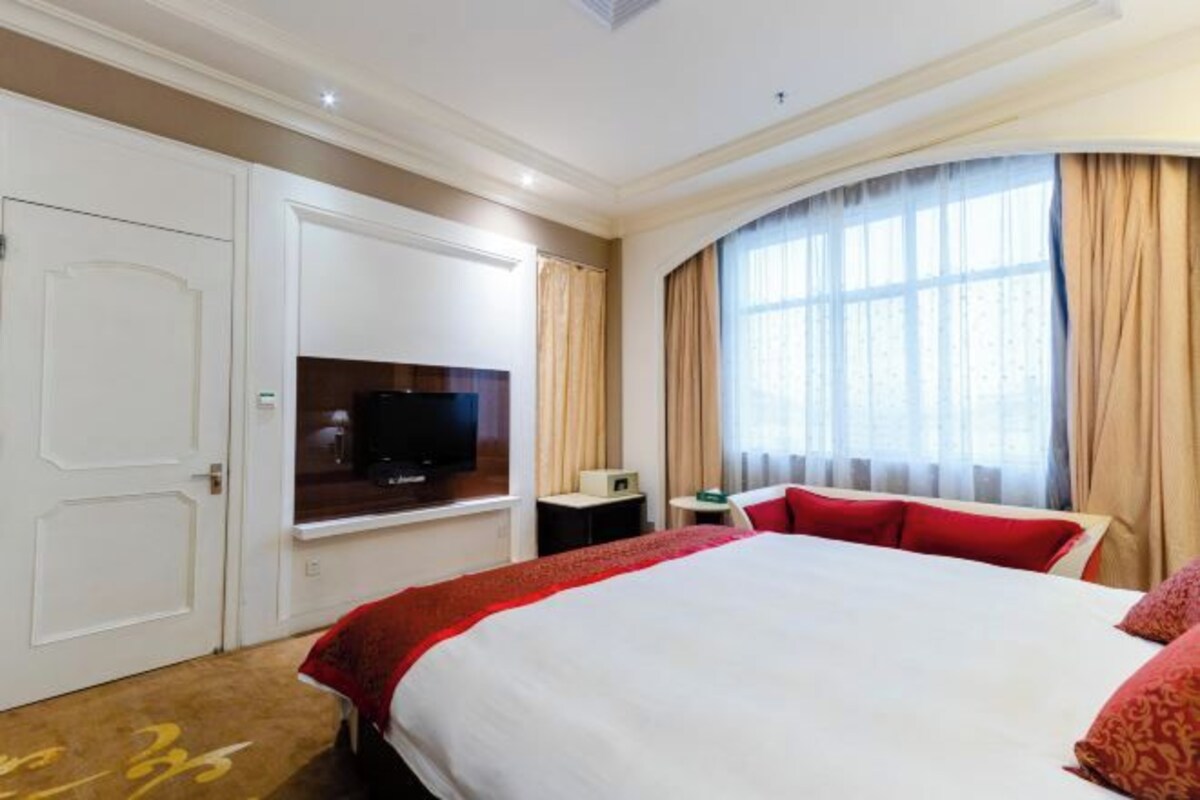 Une chambre d’hôtel avec un grand lit, une télévision, un bureau et une fenêtre avec des rideaux.