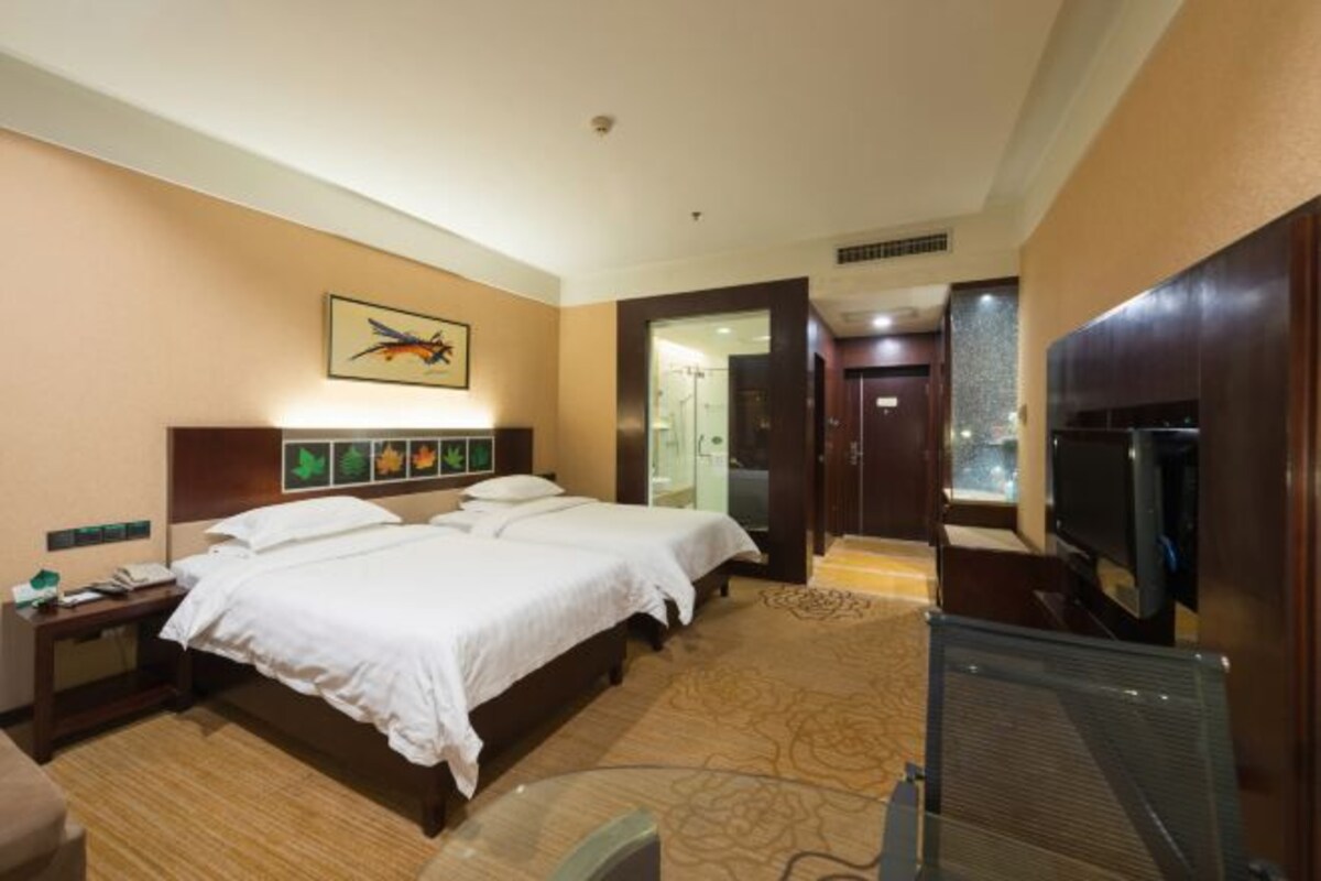 Une chambre d’hôtel avec deux lits, un bureau, une télévision et une salle de bain visible à travers une porte ouverte.