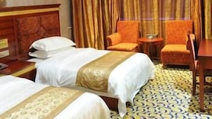 A hotel room with two beds, a wooden headboard, a small table, two chairs, and a patterned carpet. - Nanyue Tianji Taoyuan Hotel (Hengyang)