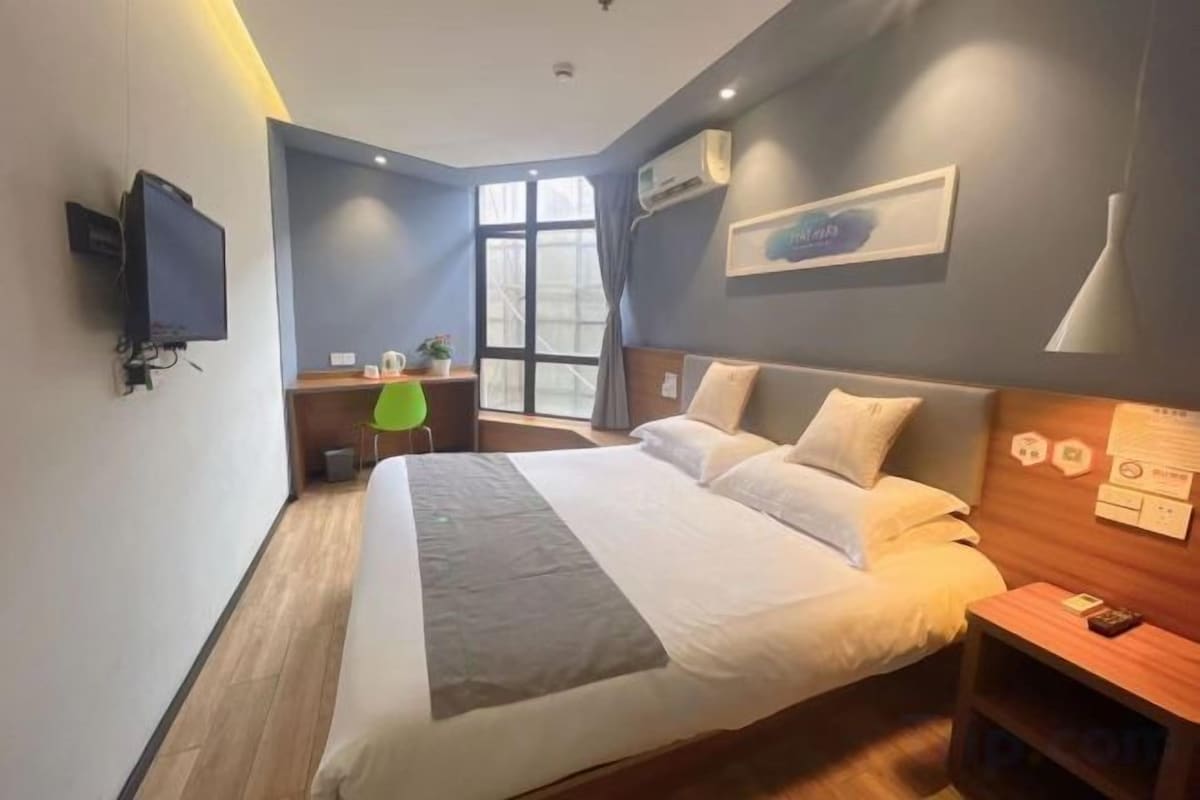 A hotel room with a large bed, a desk with a chair, a television, and a window.