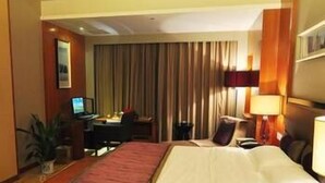 A hotel room with a large bed, a desk with a computer, a chair, a lamp, and a plant. - Fenglin International Hotel (Yulin)
