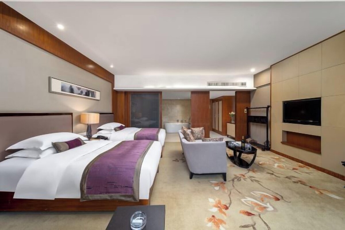 A hotel room with two beds, a sofa, a TV, and a carpeted floor.