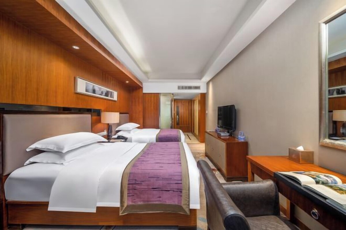 A hotel room with two beds, a desk, a chair, a television, and a minibar.
