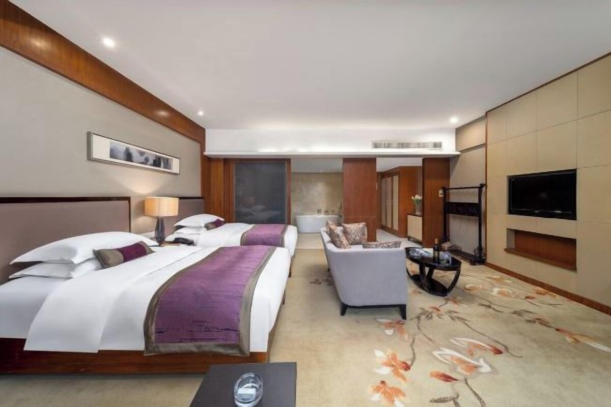 A hotel room with two beds, a sofa, a TV, and a carpeted floor.