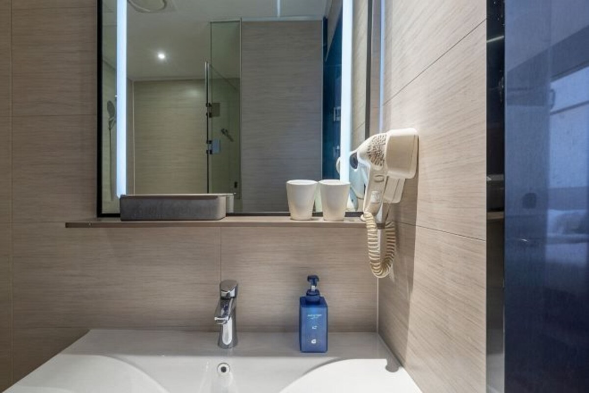 A bathroom with a sink, mirror, and hairdryer on a wall.