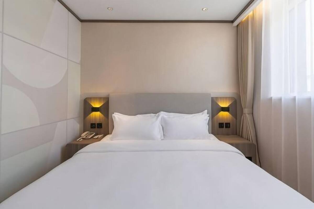 Une chambre d’hôtel avec un grand lit, deux lampes de chevet, un téléphone et une fenêtre avec des rideaux.
