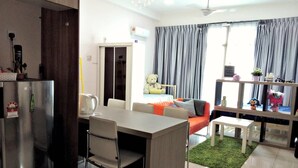 A modern living room with a sofa, dining table, and chairs. There is a kitchen area with a refrigerator and a kettle. - HomeStay in Johor - Palazio (Johor Bahru)