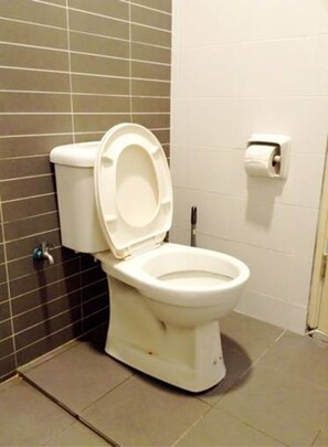 A standard white toilet with a closed lid, positioned against a wall with dark and light gray tiles. - HomeStay in Johor - Palazio (Johor Bahru)