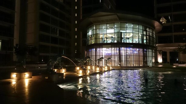A modern hotel with a circular glass facade and a water feature in the foreground. - HomeStay in Johor - Palazio (Johor Bahru)