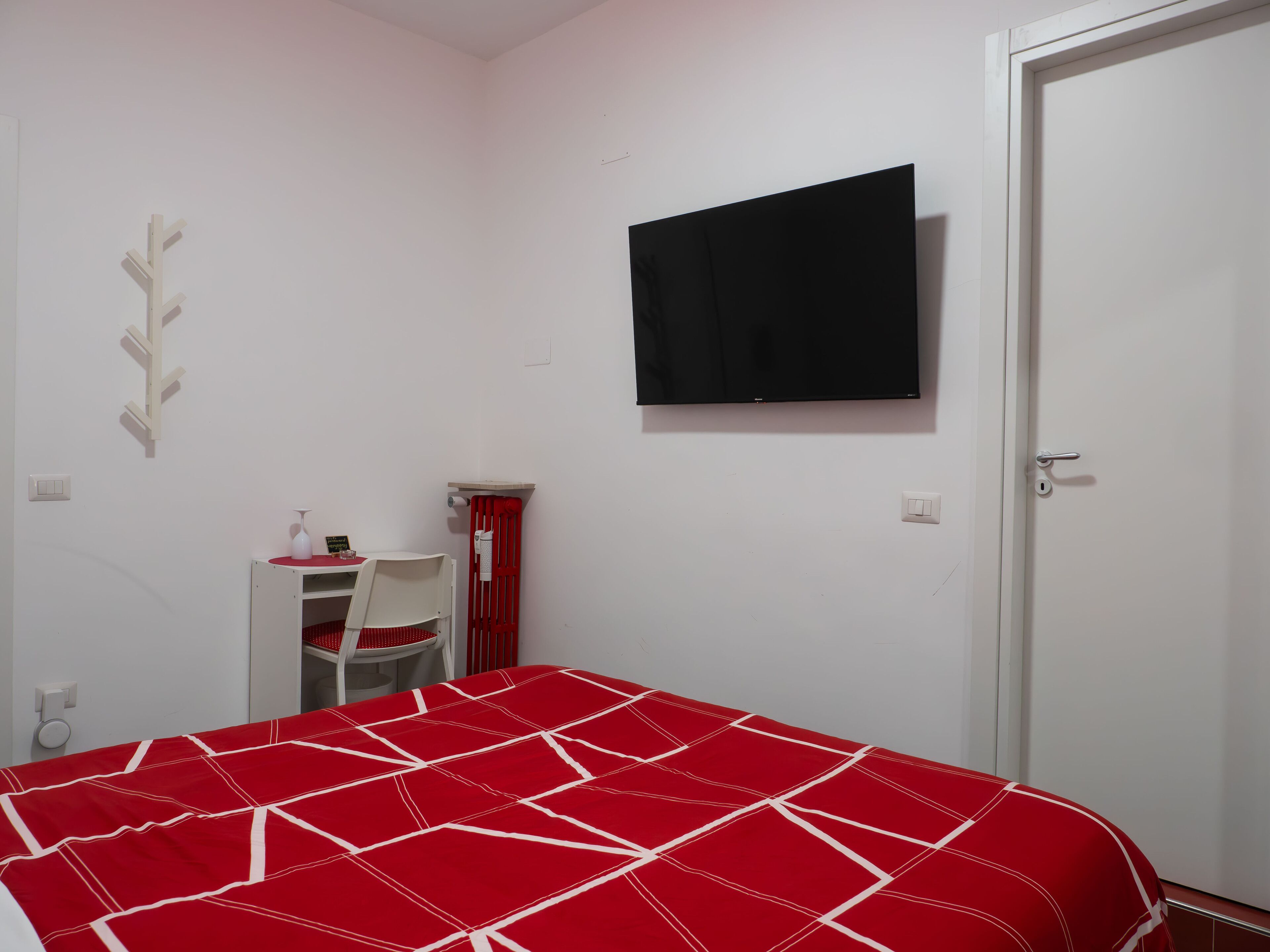 A bedroom with a bed, a desk, a chair, a TV, and a door.