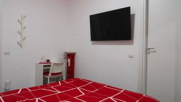 Un dormitorio con cama, escritorio, silla, televisor y puerta.