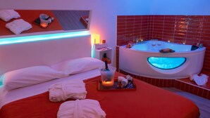 A hotel room with a red bedspread, a large white bathtub with a blue light, and neatly folded towels on the bed. - B&B Easy (Rome)