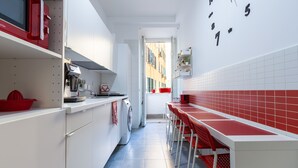 A narrow kitchen with white cabinets, a red appliance, and a red chair at the counter. - B&B Easy (Rome)