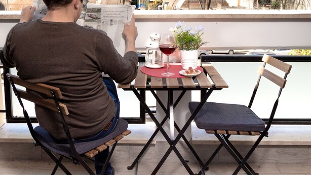 A man reading a newspaper at a table with a view of the city. - B&B Easy (Rome)