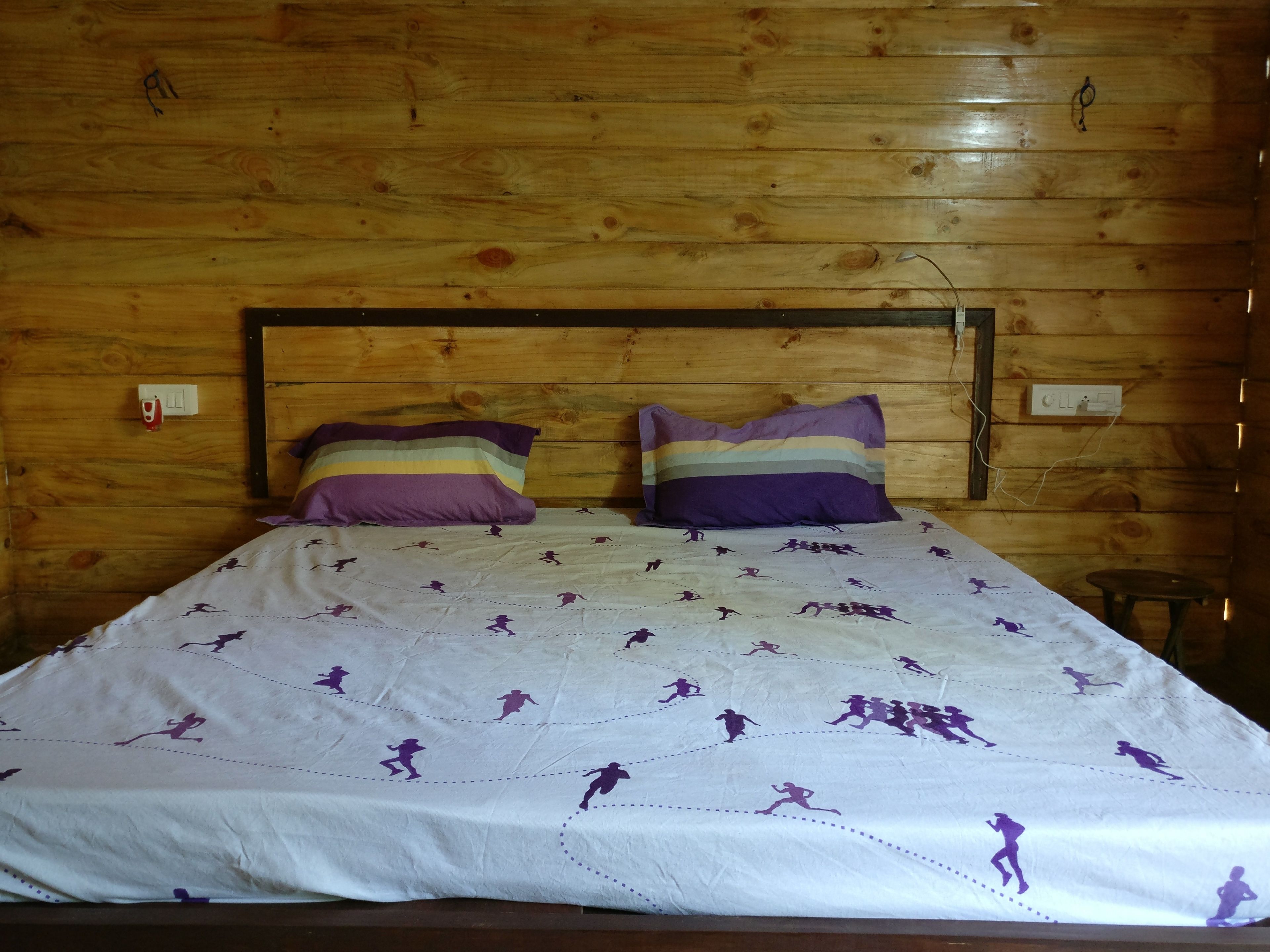 Una habitación con paneles de madera y una cama con colcha blanca con siluetas púrpuras y almohadas a rayas.