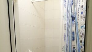 A shower area with a white tiled wall, a white door with a black frame, a white grab bar, and a shower curtain with a blue and white pattern. - Ostello Le Stanze del Sogno (Benevento)