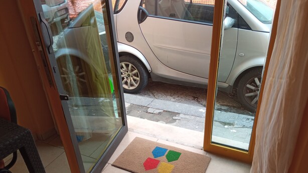 A room with a sliding glass door leading to a street, a doormat with a colorful design, and a chair. - Ostello Le Stanze del Sogno (Benevento)