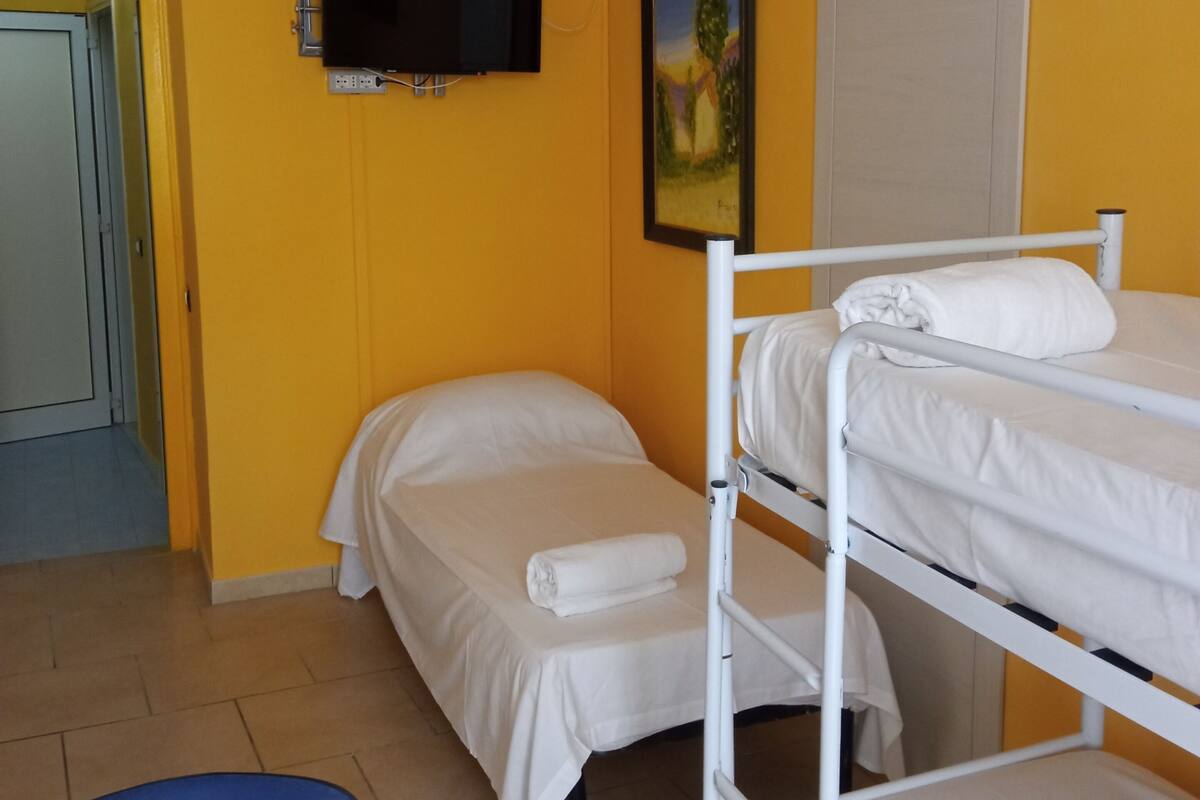 A room with yellow walls, a bed, a bunk bed, a TV, a painting, and a door.