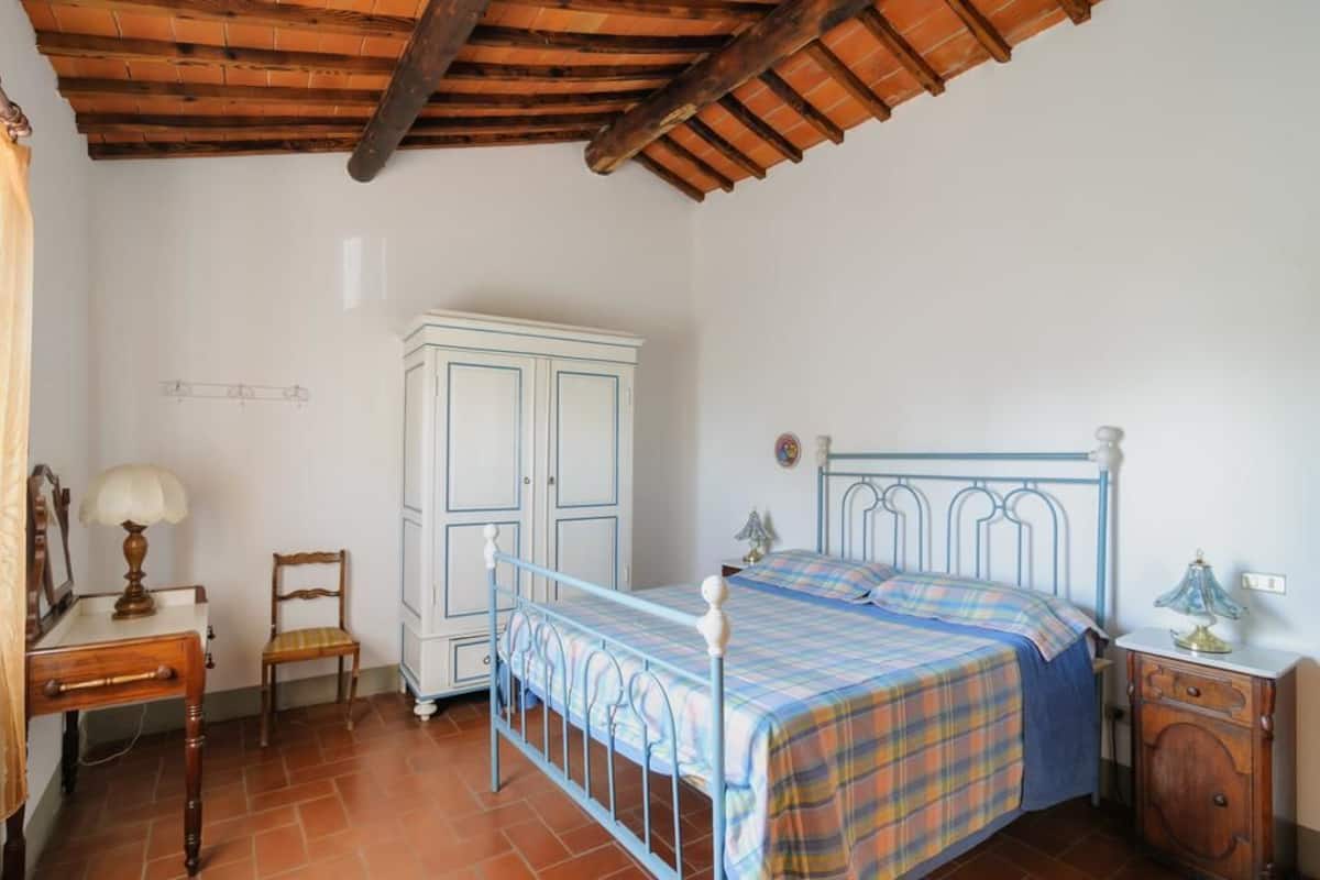 A bedroom with a bed, wooden nightstand, chair, wardrobe, and a lamp.