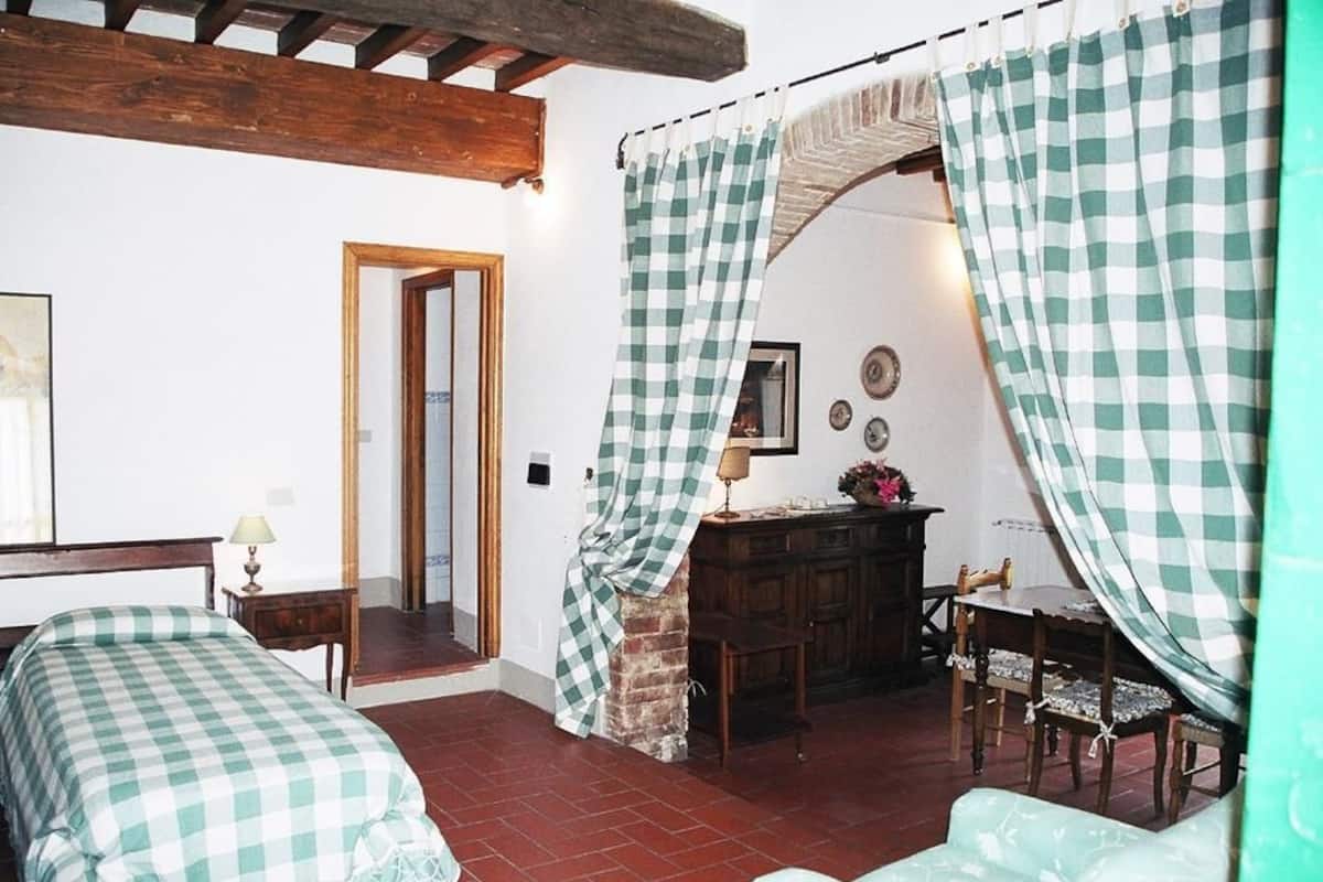 A bedroom with a checkered bedspread, a wooden headboard, a nightstand with a lamp, and a small table with chairs.