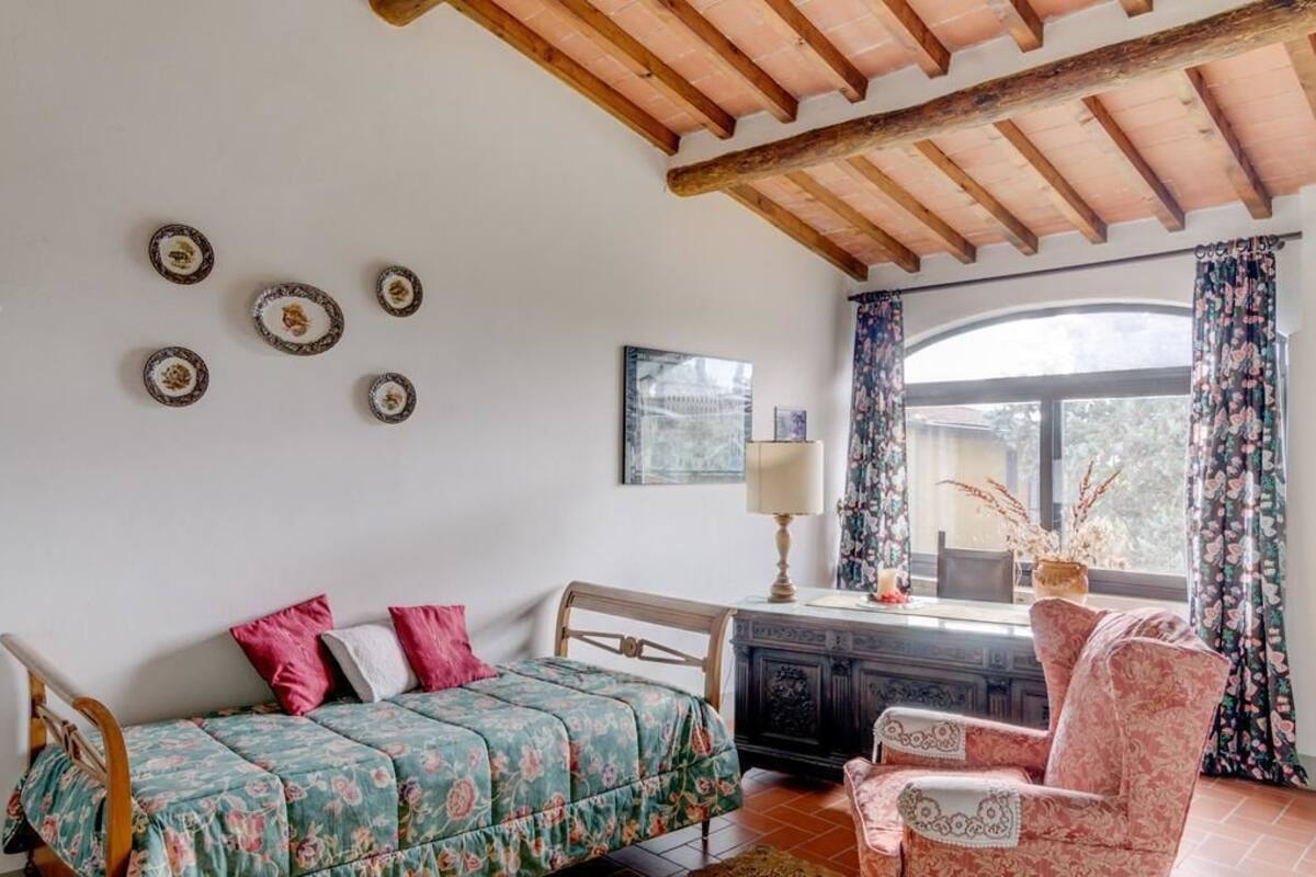 A bedroom with a bed, a chair, a window with curtains, a lamp, and wall decor.