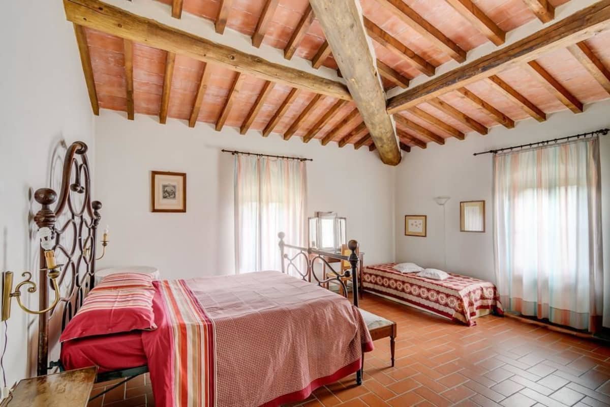 A bedroom with two beds, wooden beams, tiled floor, and curtains.
