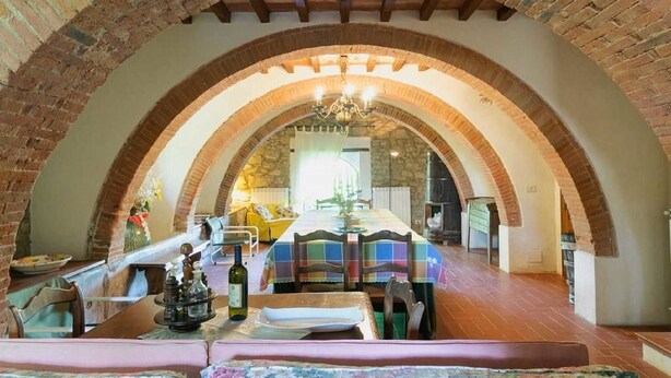 A dining area with a brick arch ceiling, a chandelier, and a table set for a meal. - Villa Albergotti (Arezzo)