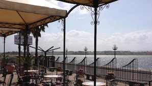 Une terrasse extérieure avec des tables et des chaises, une vue sur la mer et un panneau indiquant la présence d’un hôtel.