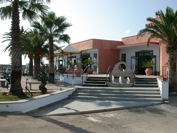 Un bâtiment à la façade rouge, bordé de palmiers et agrémenté d’une fontaine.