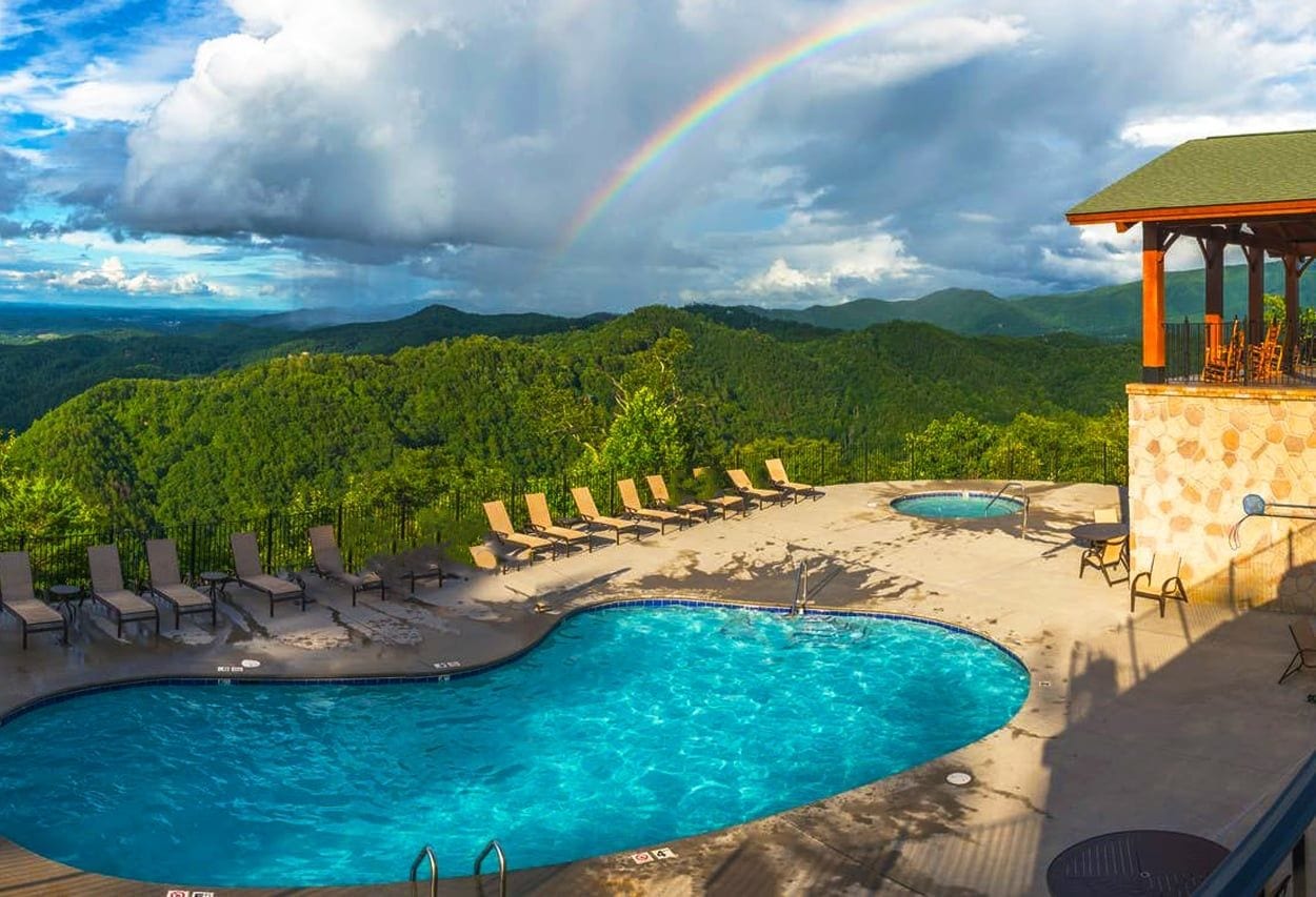 A swimming pool with lounge chairs, a gazebo, and a view of a forested mountain range.