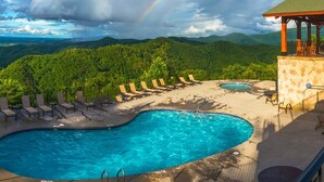 A swimming pool with lounge chairs and a gazebo, surrounded by lush greenery and a mountain view.
