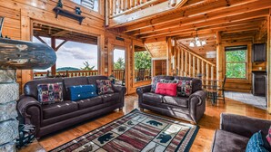 A log cabin interior with two leather sofas, a patterned rug, and a wooden staircase.
