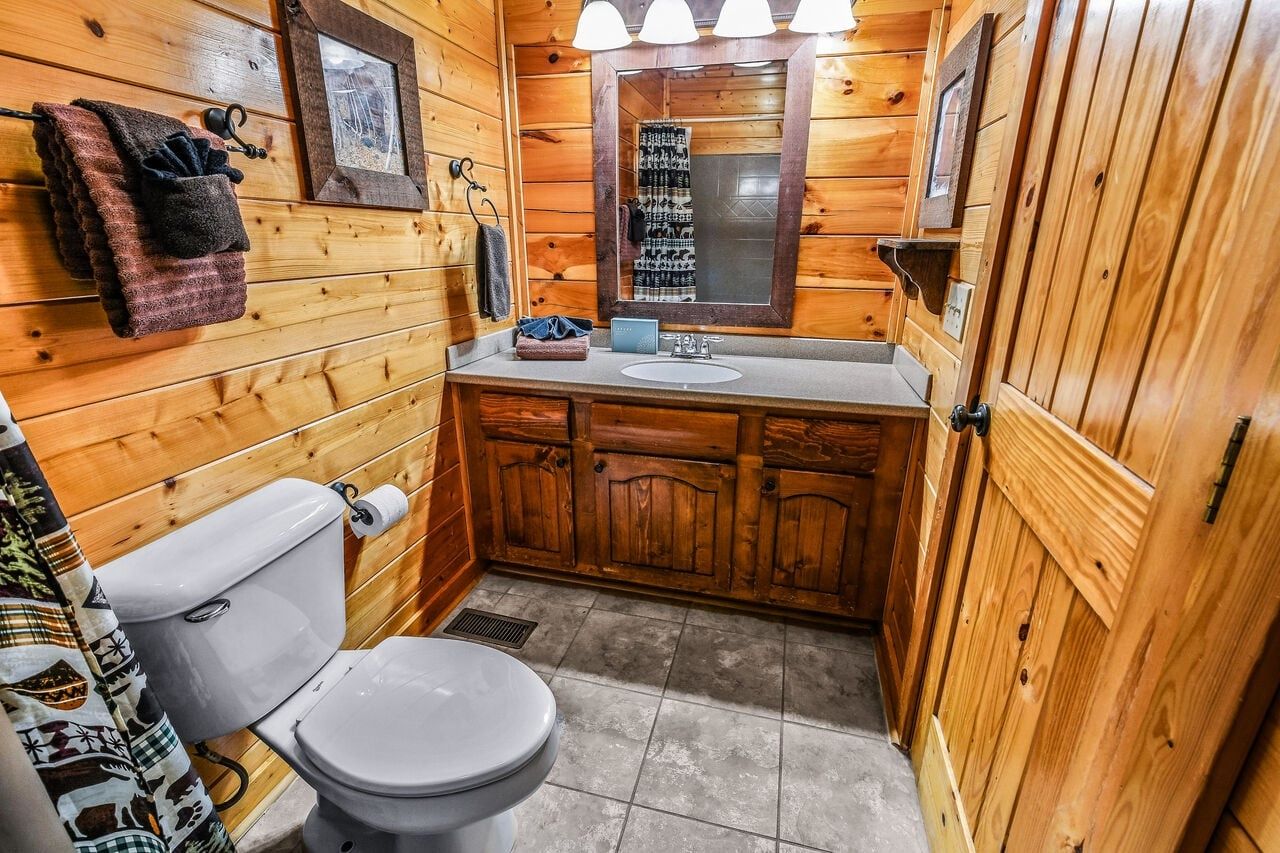 A wooden cabin bathroom with a toilet, sink, and cabinets.