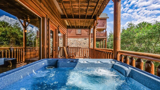 A hot tub on a wooden deck with a stone wall backdrop and a wooden railing.