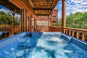 Un jacuzzi en una terraza de madera, con un muro de piedra de fondo y barandilla de madera.