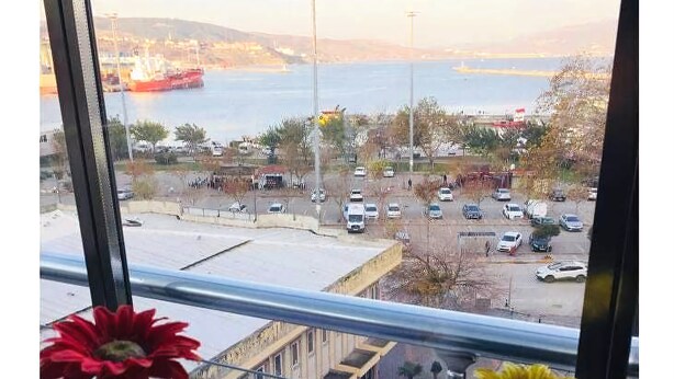 A view from a window with a clear glass pane, a parking lot, and a body of water in the background. - Tum Hotel (Bandirma)