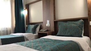 A hotel room with two beds, each with a patterned bedspread and matching pillows. There is a nightstand with a telephone and a wall-mounted light. - Tum Hotel (Bandirma)