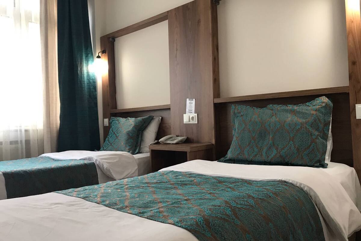 Habitación de hotel con dos camas, cada una con una colcha estampada y almohadas a juego. Hay una mesita de noche con un teléfono y una lámpara de pared.