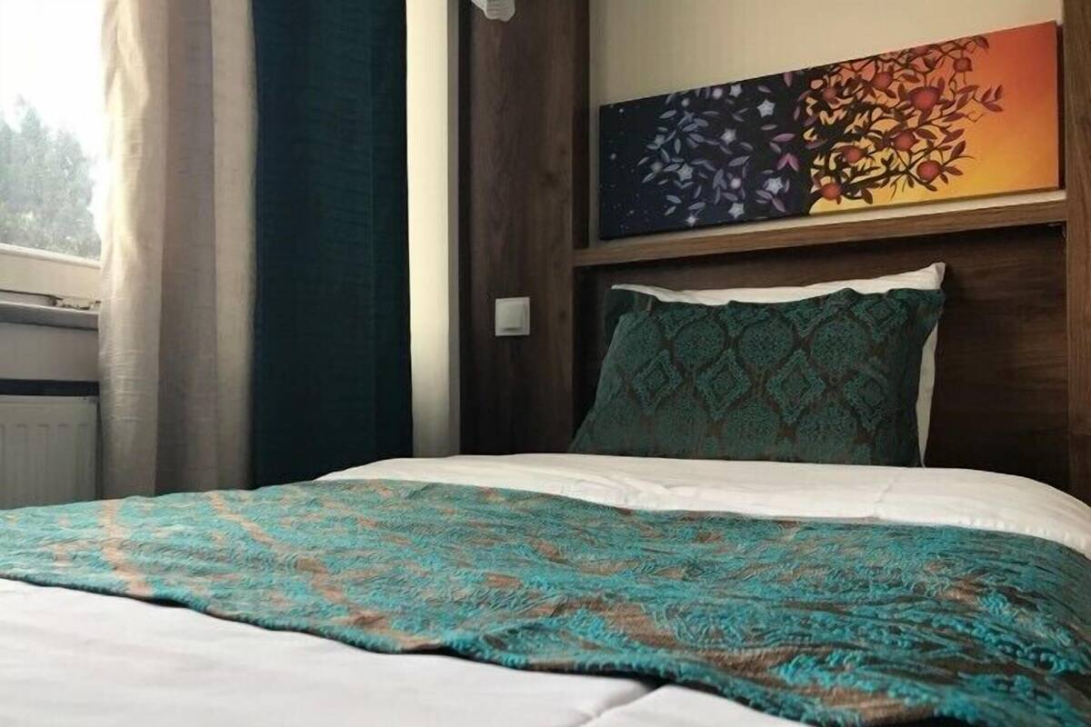 Una cama bien hecha con un edredón estampado, un cabecero oscuro y un cuadro en la pared.