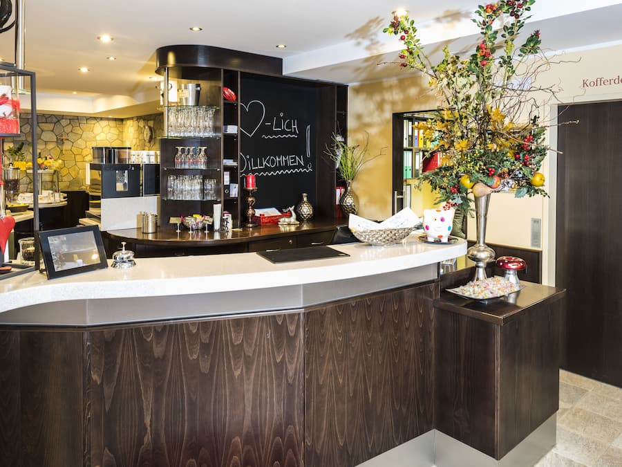 Un espace d’accueil au design moderne, comprenant un comptoir avec des verres, un tableau noir affichant un message de bienvenue et une composition florale décorative.
