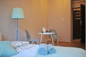 Ett hotellrum med en säng, två stolar, ett litet bord med en tekanna, koppar och en lampa.