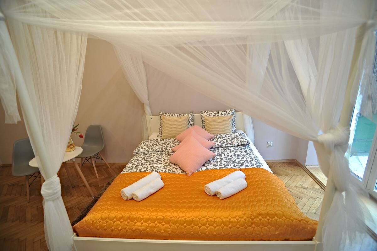 A bed with a canopy, a small table with a vase, and a chair.